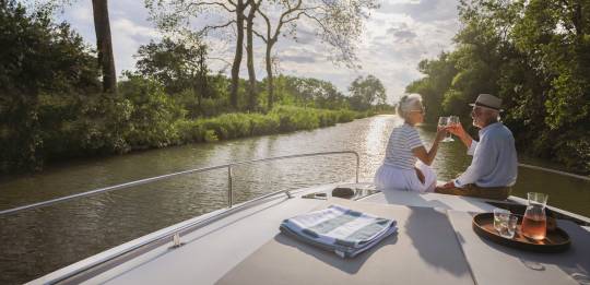 Romantic sunset moment for a couple enjoying drinks at the front of their boat on a peaceful canal.